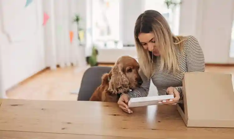 woman showing her pet dog an item from packaging |